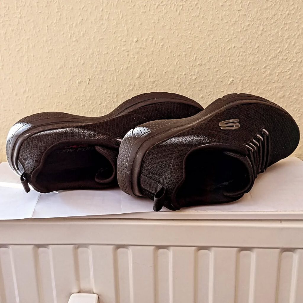 Auf einem Heizkörper liegen zwei schwarze, nasse Stoffschuhe