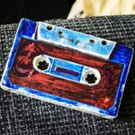 eine alte Musikkassette mit roten Ettikett wurde mit einem blauen Edding übermalt. Die Kassette sieht sehr alt aus. man sieht unter dem blauen Gekritzel den Schriftzug "Rolfs Schulweg Hitparade"