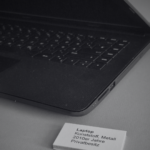 SchwarzWeiss-Foto von einem Laptop in einer Vitrine. Dazu ein kleines Schild mit dem Text: Laptop Kunststoff metall 2010er Jahre Privatbesitz